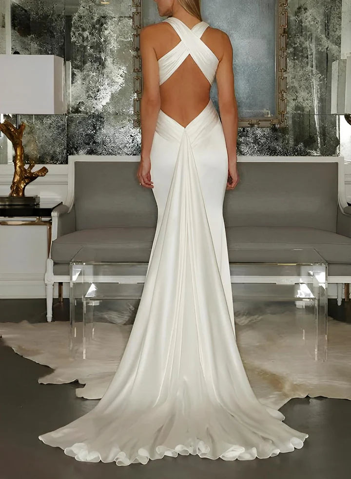 Lujoso vestido de novia color marfil de corte sirena, largo hasta el suelo, con cuello halter, escote en V profundo, detalle torcido al frente, espalda cruzada y cola capilla