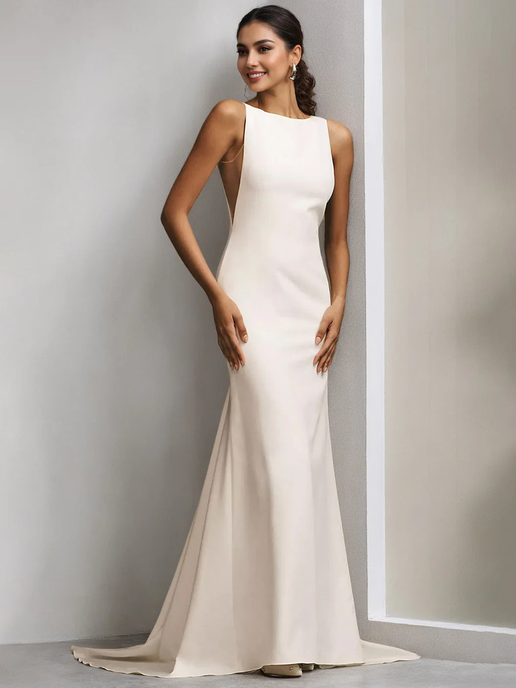 Vestido de novia moderno y minimalista color marfil, de corte sirena y largo hasta el suelo, con escote barco, sin mangas, espalda pronunciada y cola de capilla