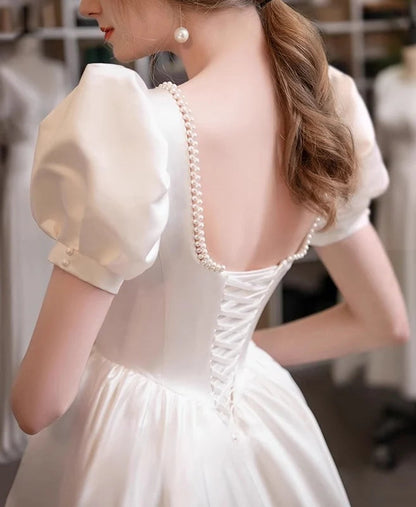 Vestido de novia de satén con escote cuadrado, mangas abullonadas, ribete de perlas, espalda con cordones y falda en línea A