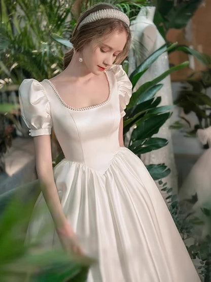 Vestido de novia de satén con escote cuadrado, mangas abullonadas, ribete de perlas, espalda con cordones y falda en línea A